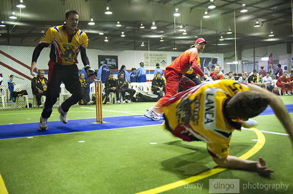 Indoor Cricket wicket keeper and front half fielder diving towards camera to field ball.